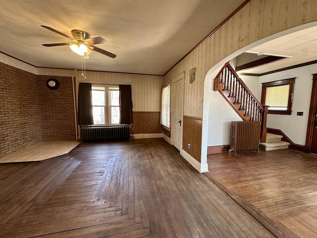 unfurnished living room with a wainscoted wall, radiator heating unit, arched walkways, and crown molding