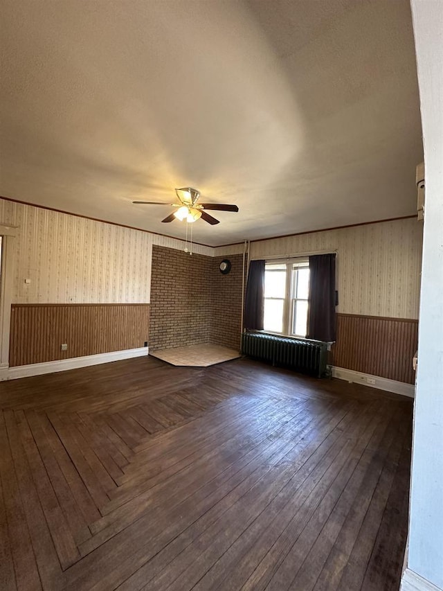 spare room featuring a wainscoted wall, radiator, wood-type flooring, a ceiling fan, and wallpapered walls