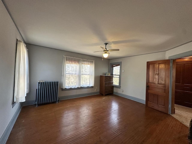 unfurnished bedroom featuring a ceiling fan, radiator heating unit, baseboards, and wood finished floors