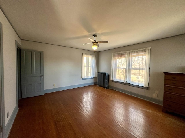 unfurnished bedroom featuring radiator, ceiling fan, baseboards, and wood finished floors