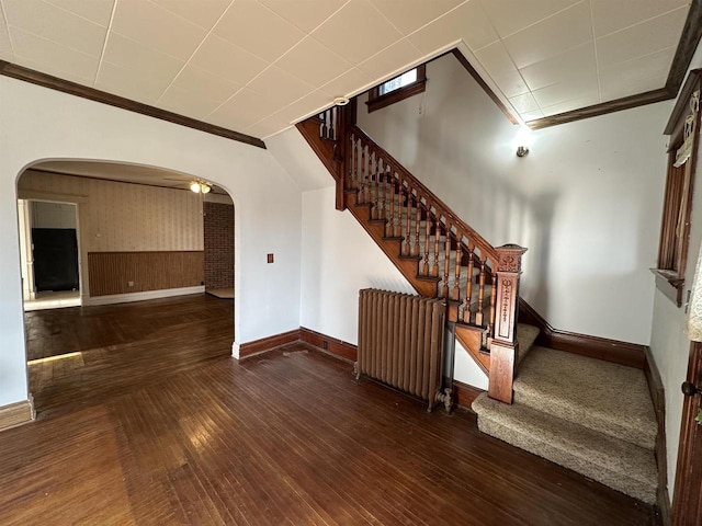 interior space featuring ornamental molding, arched walkways, radiator, and wood finished floors