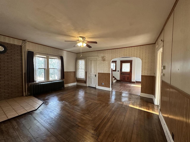 foyer featuring a wainscoted wall, radiator heating unit, arched walkways, and hardwood / wood-style flooring