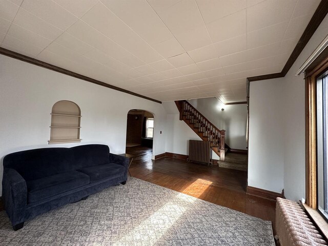 living room with arched walkways, crown molding, radiator, wood finished floors, and stairs