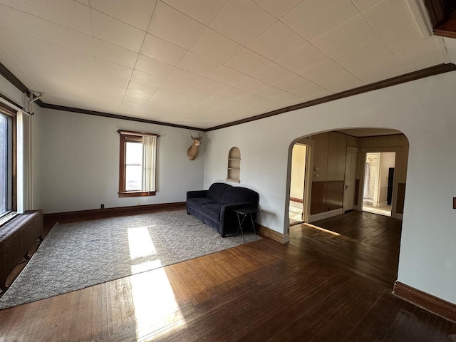 unfurnished room with dark wood-style floors, arched walkways, crown molding, and baseboards