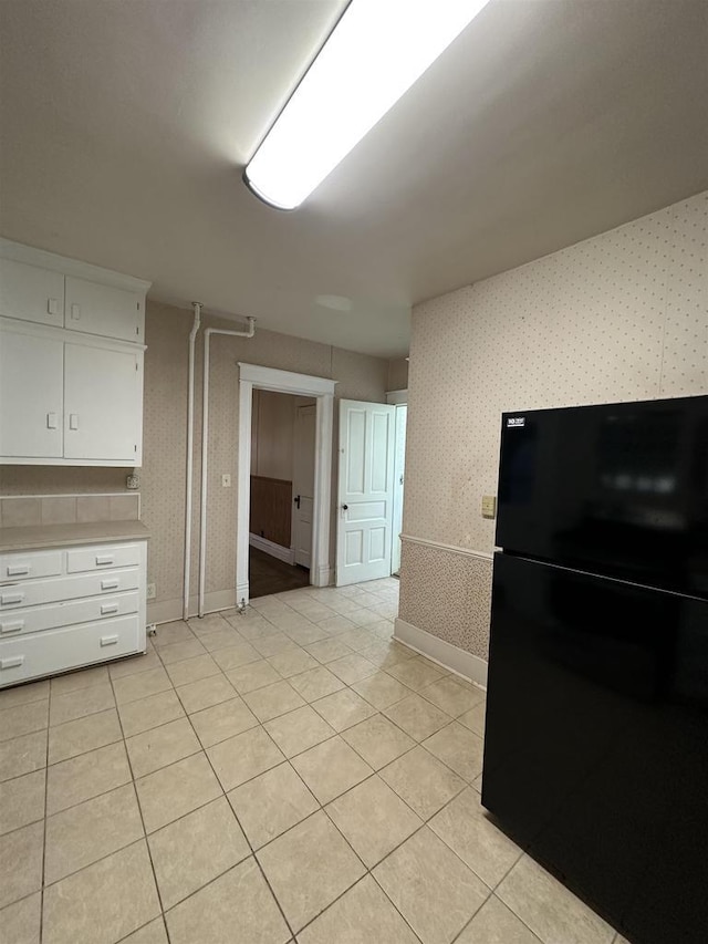 kitchen featuring light countertops, freestanding refrigerator, white cabinetry, light tile patterned flooring, and wallpapered walls