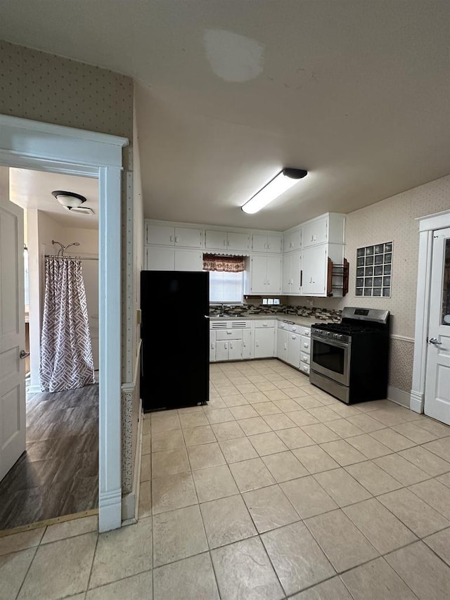 kitchen with freestanding refrigerator, white cabinets, stainless steel gas stove, and wallpapered walls