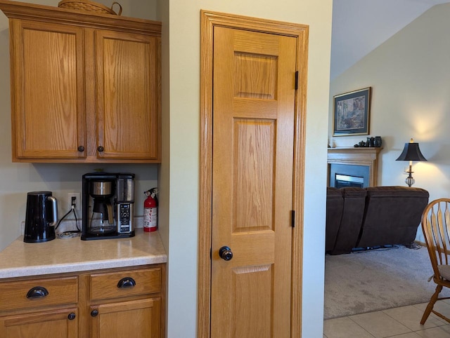 kitchen with brown cabinets, light colored carpet, light countertops, and a fireplace