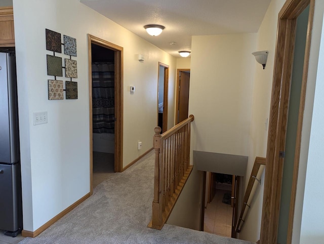 corridor with baseboards, carpet flooring, and an upstairs landing