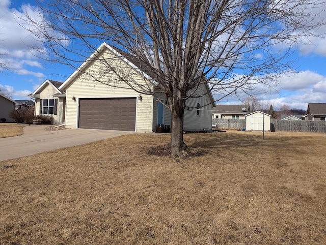 view of front of home with concrete driveway, a front yard, fence, a shed, and a garage