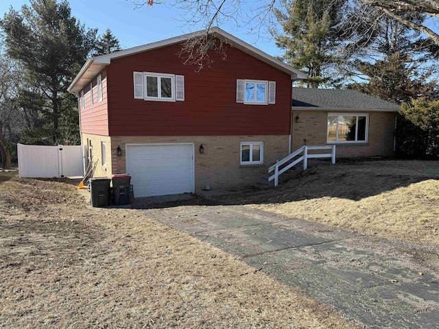 tri-level home featuring brick siding, fence, driveway, and an attached garage