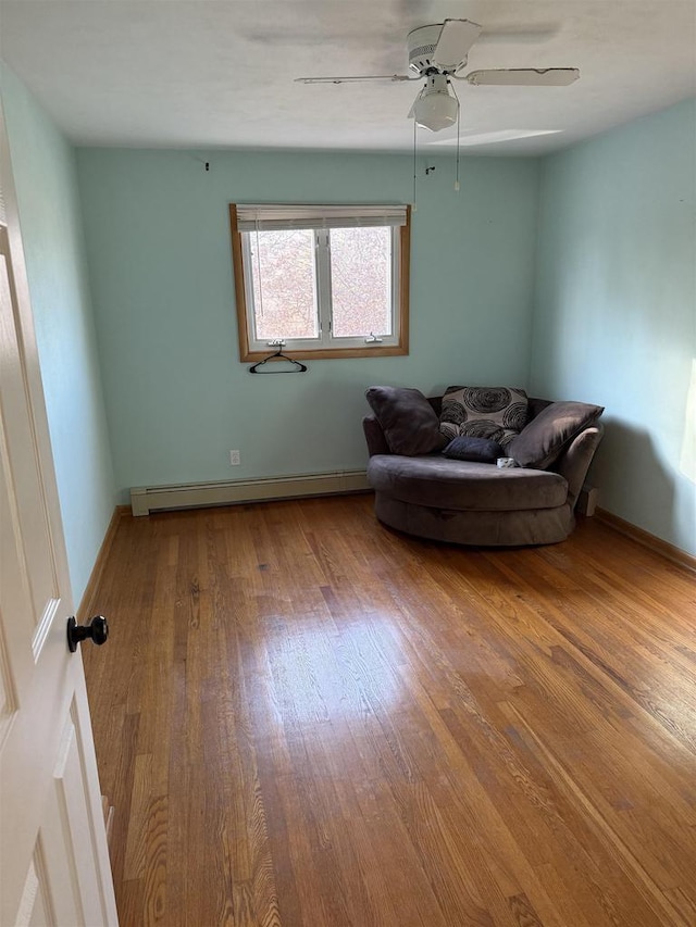 sitting room with a ceiling fan, baseboards, a baseboard heating unit, and wood finished floors