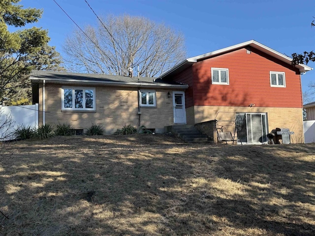 rear view of house featuring entry steps, brick siding, a yard, and fence