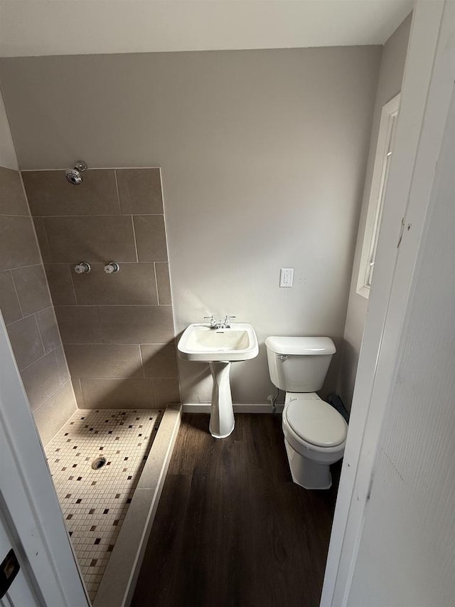 full bathroom featuring toilet, baseboards, a tile shower, and wood finished floors