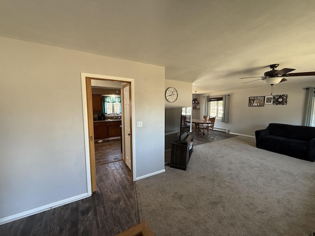 unfurnished living room with dark carpet, a sink, a ceiling fan, and baseboards