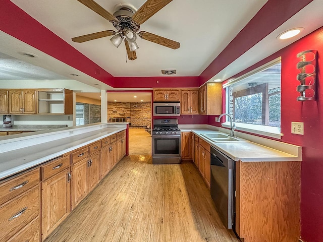 kitchen with stainless steel appliances, a sink, light countertops, light wood-type flooring, and brown cabinetry