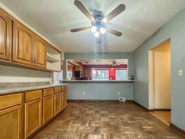 kitchen featuring baseboards, visible vents, brown cabinetry, stainless steel microwave, and a textured ceiling