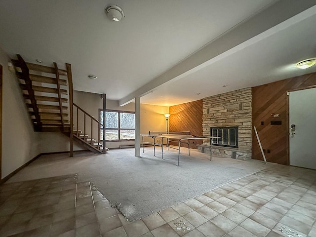 unfurnished living room featuring beamed ceiling, stairs, carpet floors, wood walls, and a fireplace