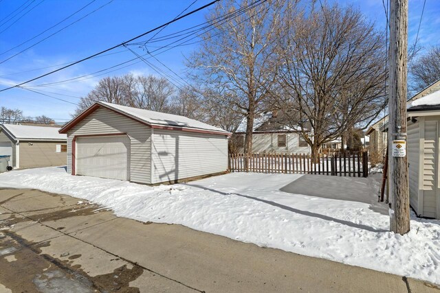 snow covered garage featuring a garage and fence