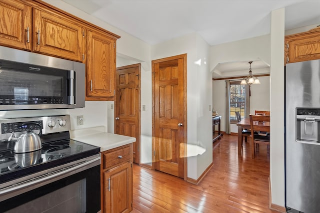 kitchen featuring a notable chandelier, stainless steel appliances, light countertops, light wood-type flooring, and brown cabinetry