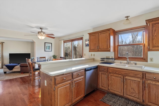 kitchen with a peninsula, a sink, light countertops, dishwasher, and brown cabinetry