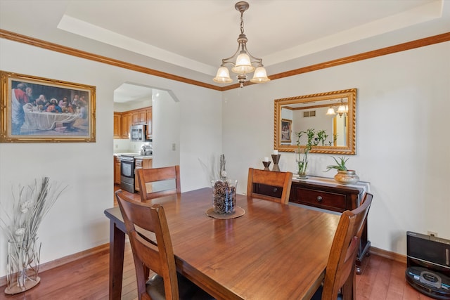 dining space with arched walkways, a tray ceiling, a notable chandelier, light wood-style floors, and baseboards