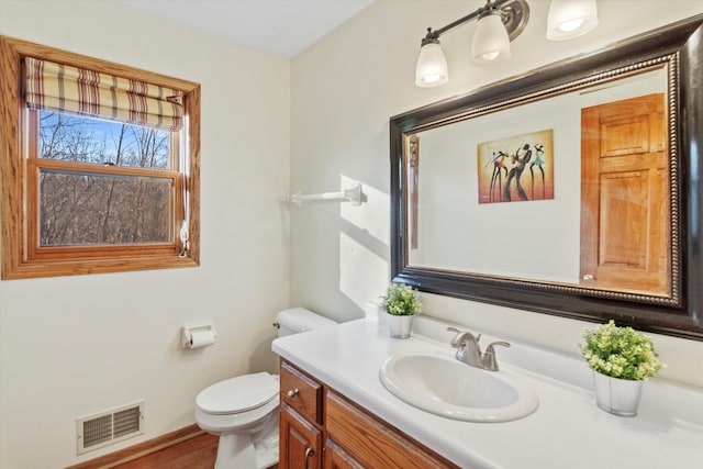 half bath featuring baseboards, visible vents, vanity, and toilet