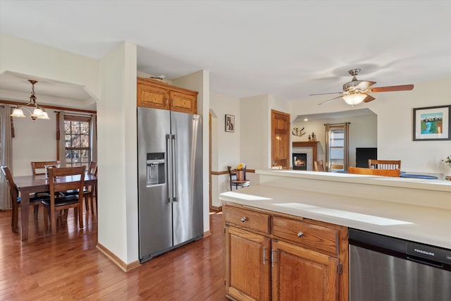 kitchen featuring stainless steel appliances, brown cabinetry, light countertops, and light wood-style flooring