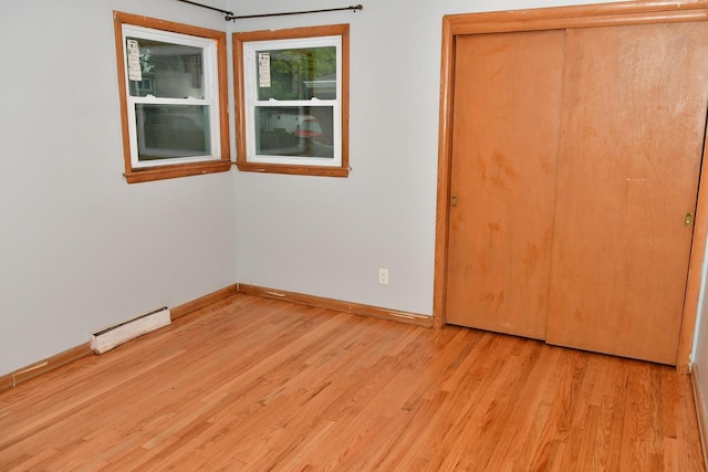 unfurnished bedroom with light wood finished floors, baseboards, a baseboard heating unit, and a closet