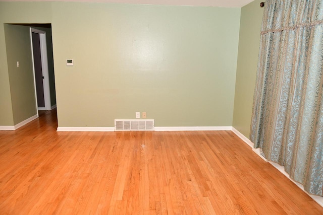 spare room with light wood-type flooring, visible vents, and baseboards