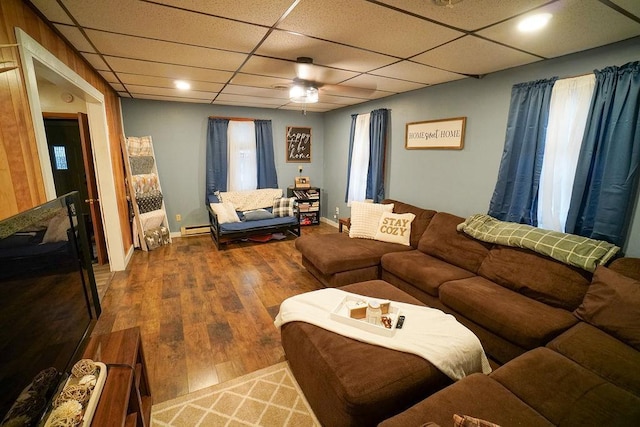 living area featuring baseboards, baseboard heating, a drop ceiling, and wood finished floors