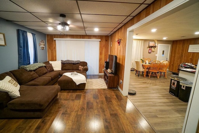 living area with wood finished floors, a paneled ceiling, and wooden walls