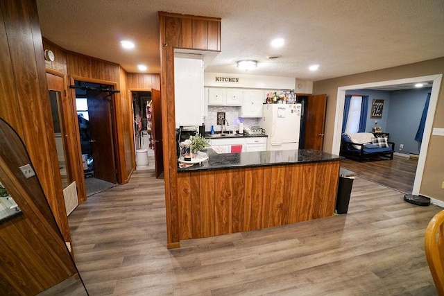 kitchen with dark countertops, freestanding refrigerator, a sink, light wood-type flooring, and a peninsula