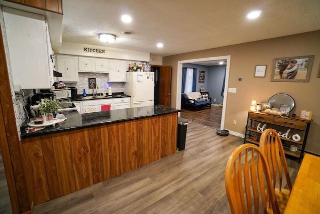 kitchen with light wood-style flooring, a peninsula, white appliances, a sink, and tasteful backsplash