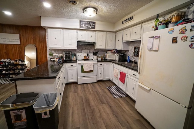 kitchen with under cabinet range hood, a peninsula, white appliances, white cabinets, and dark wood finished floors