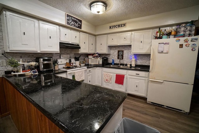 kitchen featuring under cabinet range hood, a peninsula, white appliances, a sink, and dark wood finished floors