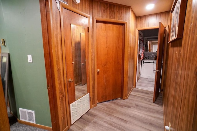 corridor featuring visible vents, wood walls, and light wood finished floors