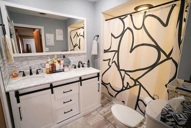 bathroom with a sink, double vanity, backsplash, and toilet