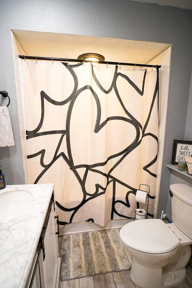 full bathroom featuring a textured wall, toilet, a shower with shower curtain, vanity, and wood finish floors