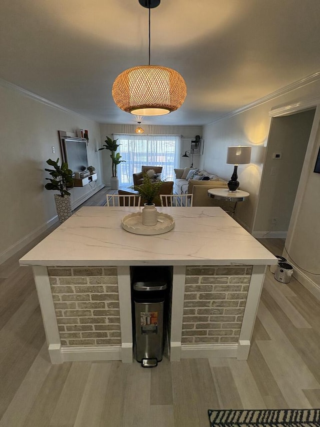 bar featuring light wood-type flooring, crown molding, hanging light fixtures, and baseboards