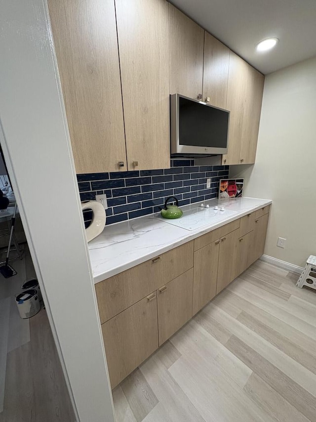 kitchen featuring light wood-style floors, light stone counters, decorative backsplash, and light brown cabinetry