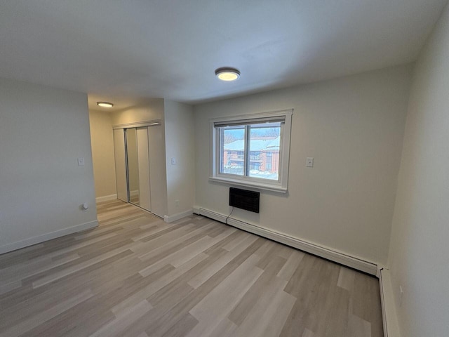 spare room with light wood finished floors, a baseboard radiator, and baseboards