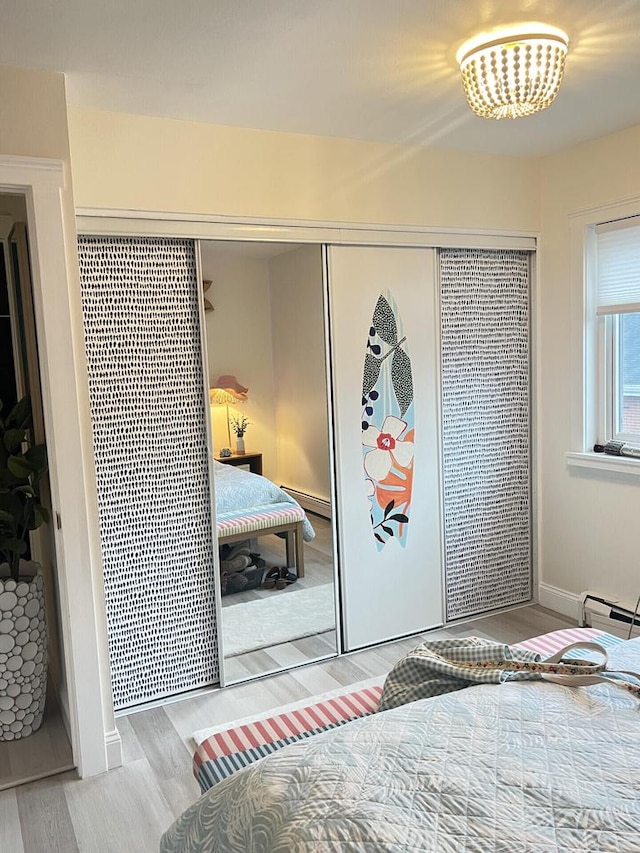 bedroom with a baseboard radiator, a closet, baseboards, and wood finished floors