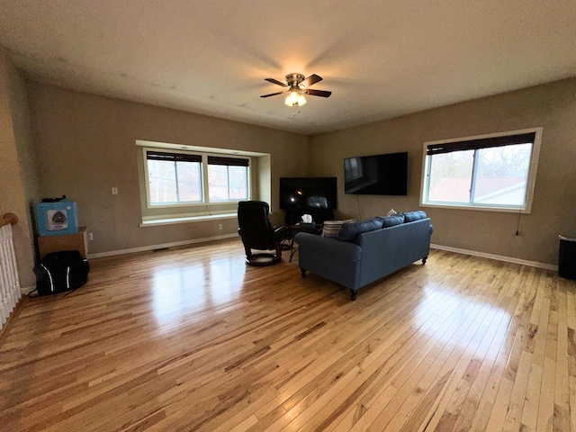 living room featuring a ceiling fan, baseboards, and light wood finished floors