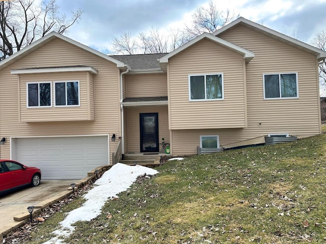 bi-level home with an attached garage, concrete driveway, a front yard, and a shingled roof