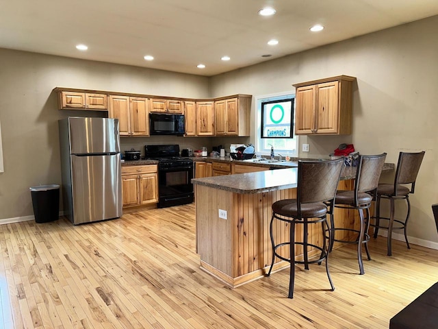 kitchen with light wood-style flooring, dark countertops, black appliances, and a peninsula