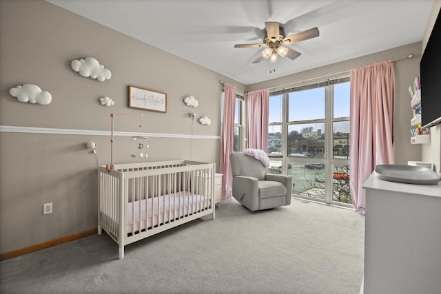 bedroom featuring a nursery area, carpet, baseboards, and ceiling fan