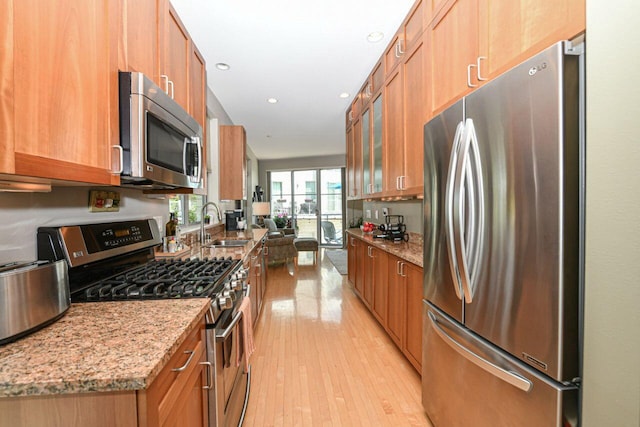 kitchen featuring brown cabinets, a sink, light stone counters, light wood-style floors, and appliances with stainless steel finishes