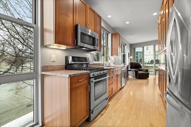 kitchen with light wood-type flooring, recessed lighting, brown cabinetry, stainless steel appliances, and a sink