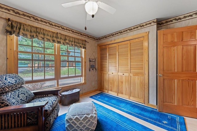 living area with a ceiling fan, wallpapered walls, and wood finished floors