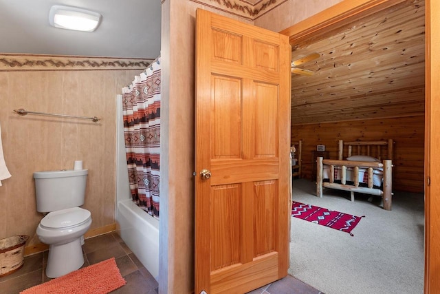 bathroom with toilet, shower / bath combo with shower curtain, vaulted ceiling, wooden walls, and tile patterned flooring